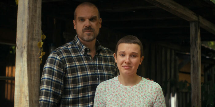 Actors Millie Bobby Brown and David Harbour on the set of Netflix&rsquo;s Stranger Things in a rustic outdoor setting.