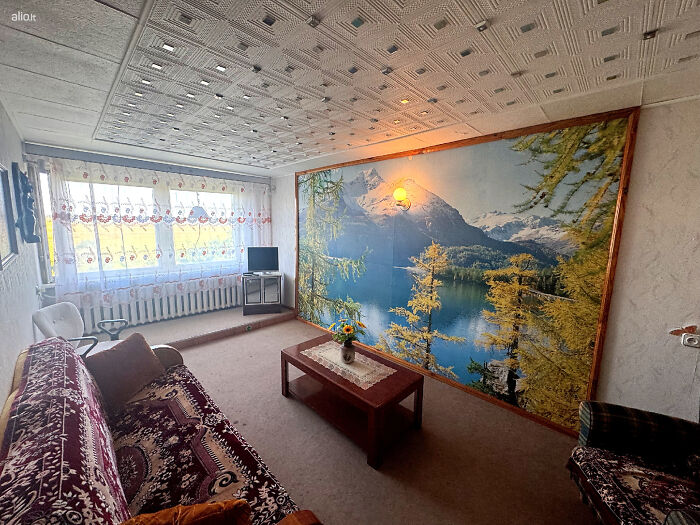 Sala de estar con decoración vintage y un gran mural de paisaje natural en listado inmobiliario entretenido.