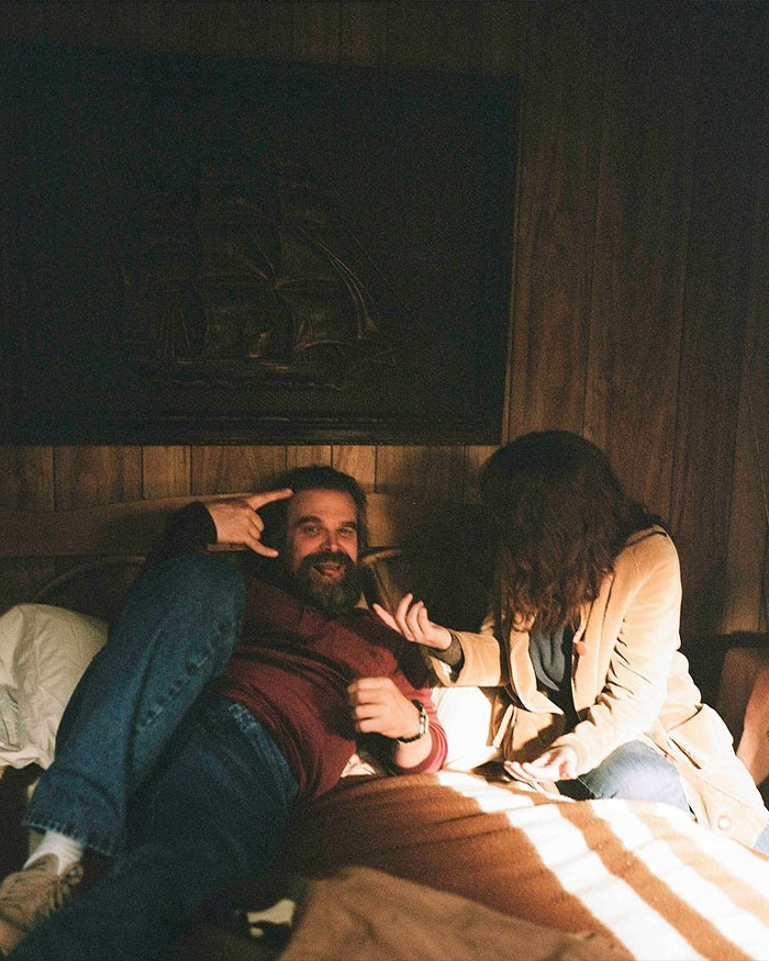 David Harbour relaxing indoors with a woman, highlighting Stranger Things co-star connection in a cozy setting.