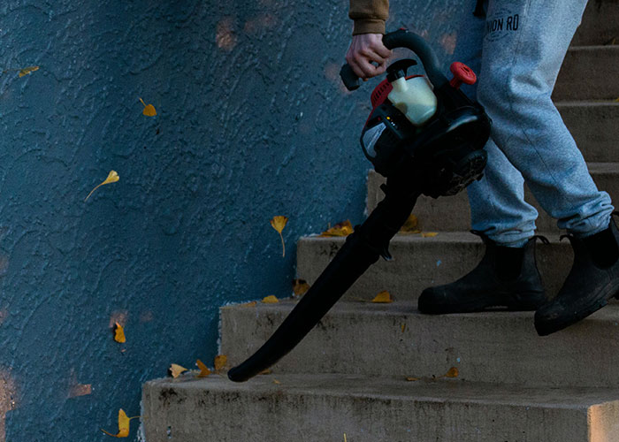 Person using a leaf blower to clean outdoor stairs demonstrating genius cleaning hacks inspired by laziness.