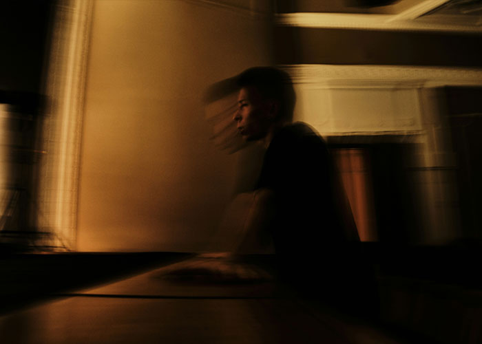 Blurred image of a young man in a dark room, reflecting the surreal theme of a man claiming a cockroach ordered him.