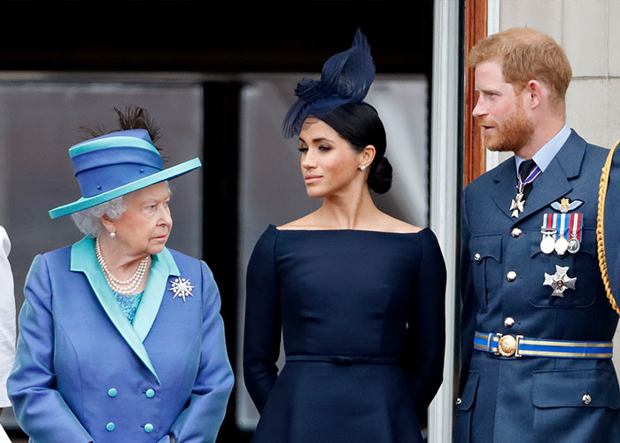 Meghan Markle in a navy dress and fascinator with Queen Elizabeth II and Prince Harry at a formal public event.