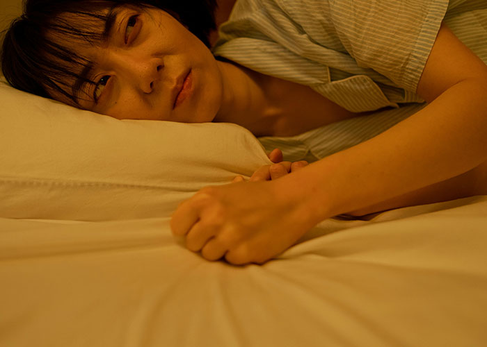 Person lying awake in bed, looking uneasy and disturbed by bizarre events during the night.