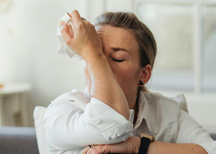 Woman in white shirt holding tissue to face, expressing frustration over receiving horrible gifts described by 91 people.