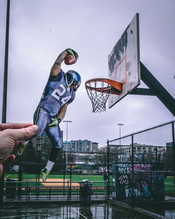 Hand holding paper cutout of football player dunking basketball on outdoor court, showcasing paper cutouts interaction.