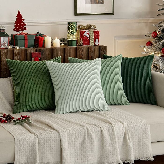 Set of green cozy pillows arranged on a beige couch with holiday decor and warm candlelight in the background.