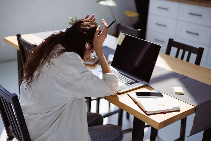Stressed woman sitting at a desk with laptop and notebook, reflecting on lessons learned from past mistakes.