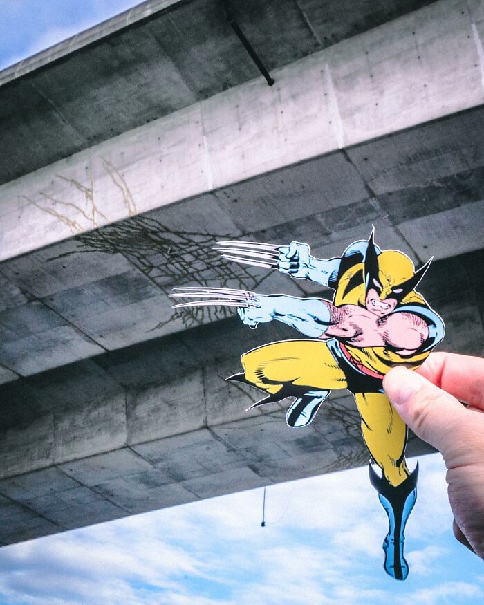 Hand holding a paper cutout of a superhero with claws, interacting with real-life concrete structures and shadows.