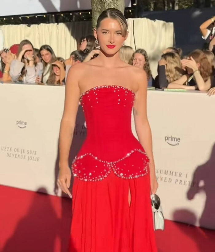 Influencer in red dress posing on red carpet, surrounded by crowd, criticized for partying while contagious and irresponsible behavior. Influencer in red dress posing on red carpet, surrounded by crowd, criticized for partying while contagious and irresponsible behavior.
