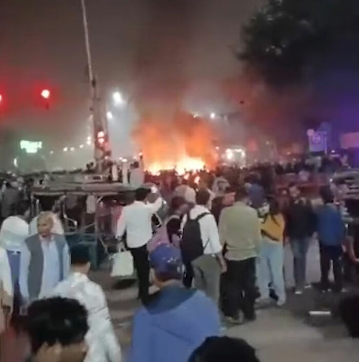 Crowd gathers near a large car blast with heavy flames and smoke in a city, illustrating horror car blast incident.