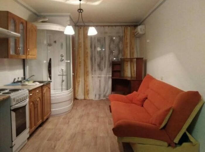 Sala y cocina integrada con sofá naranja y ducha en un espacio pequeño, listado inmobiliario entretenido y único.