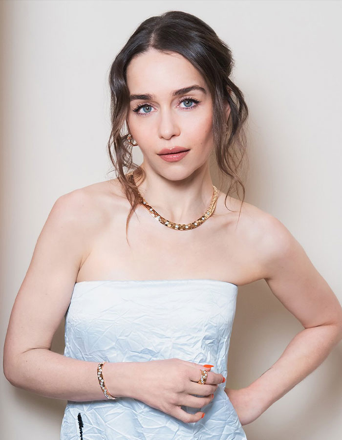 Emilia Clarke posing in a strapless dress with jewelry, highlighting discussions on same surgeries and Hollywood face changes.