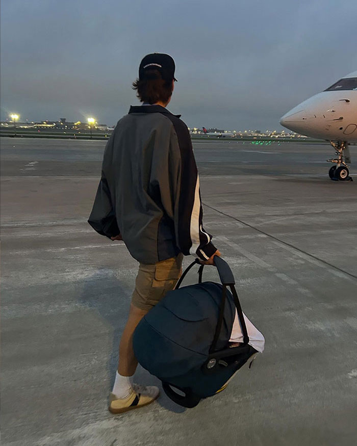 Person walking on airport tarmac carrying a baby car seat, representing Millie Bobby Brown adopting a baby at 21. Person walking on airport tarmac carrying a baby car seat, representing Millie Bobby Brown adopting a baby at 21.