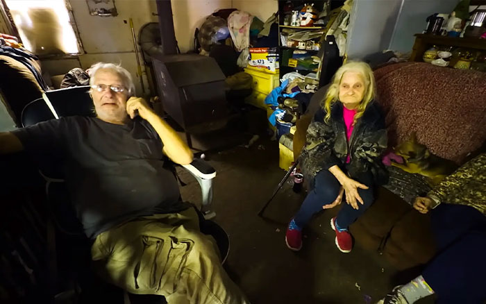 Elderly man and woman sitting in a cluttered room, part of America's most inbred family viral fame reaction.