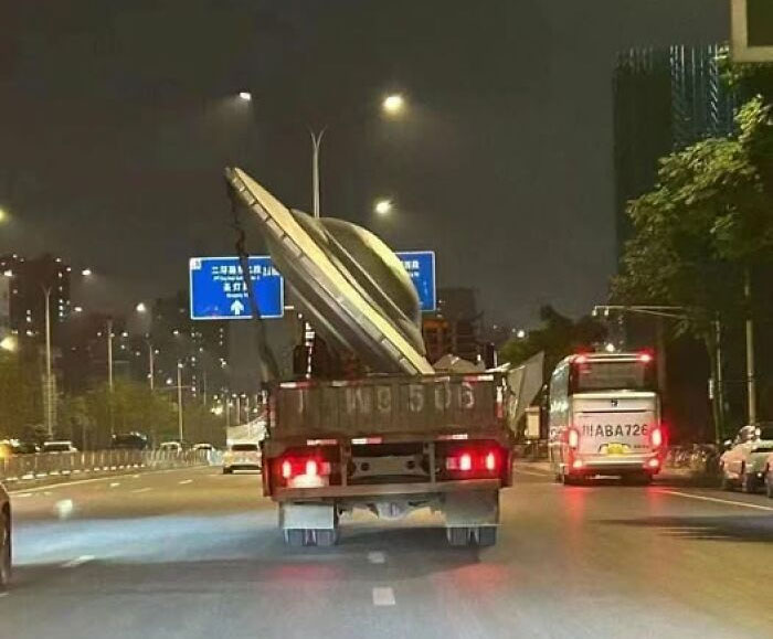 Truck carrying a large UFO prop on a city road at night, a bold and striking pic that goes hard on urban streets.