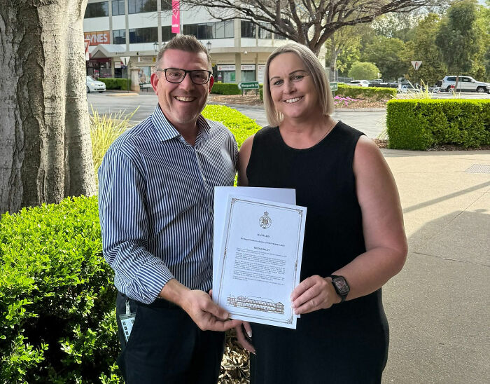 Politician smiling outdoors with a woman while holding a formal resignation document during daytime.