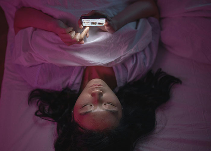 Person lying in bed using a phone with soft lighting, illustrating moments psychiatric institution workers found unforgettable on the job.