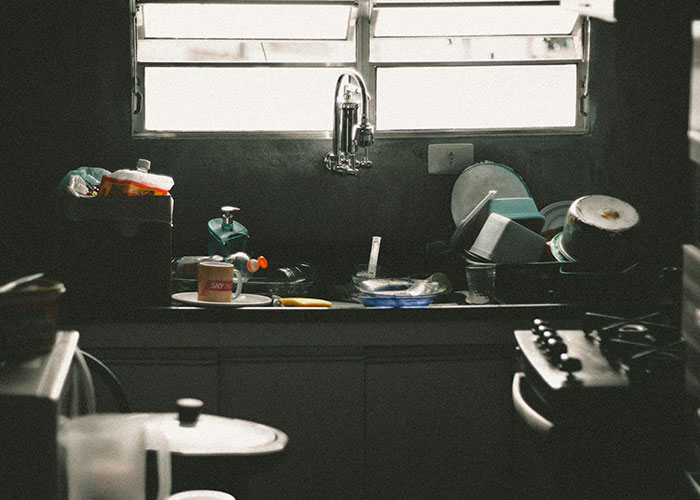 Dimly lit kitchen sink filled with dirty dishes and kitchen items, illustrating life hacks for everyday use.