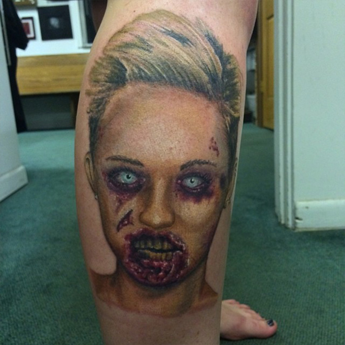 Tattoo artist regrets Miley tattoo with unsettling zombie-style face ink on a person's leg indoors.