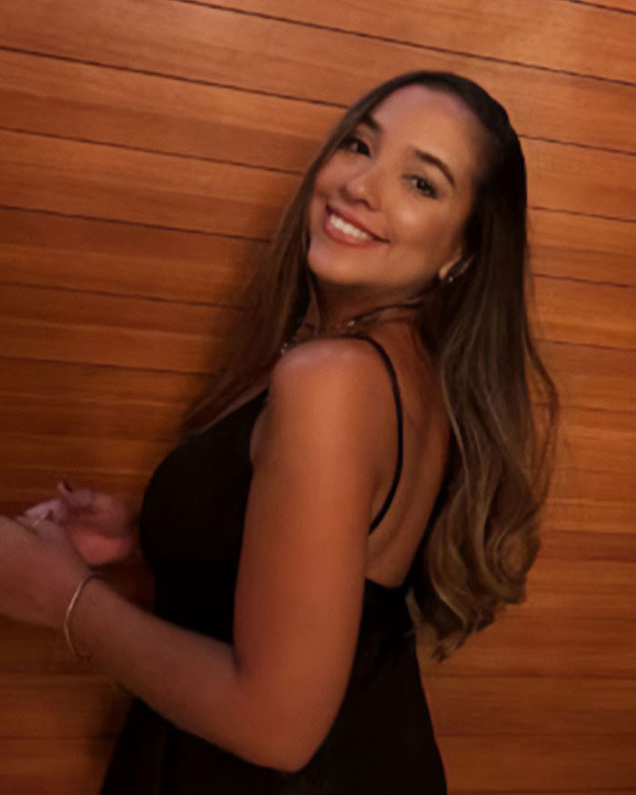 Smiling woman with long hair wearing a black dress, representing women who had a BBL and faced tragic consequences.
