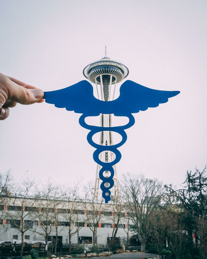 Blue paper cutout interacting with real-life Seattle Space Needle in creative art by Rudy Willingham.