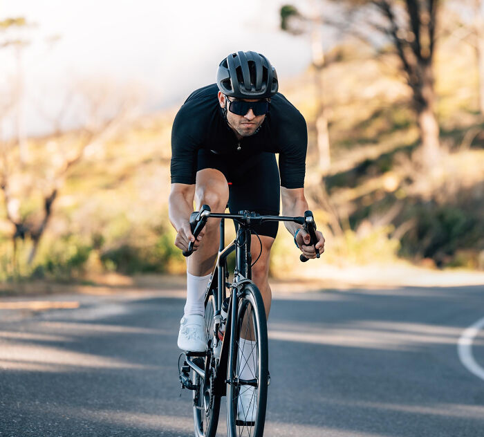 Man wearing helmet and sunglasses riding a road bike outdoors, representing stories of people who messed up once and learned.
