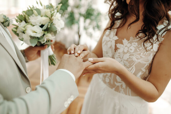 Bride placing ring on groom's finger during wedding ceremony, symbolizing lessons learned and promises never again.