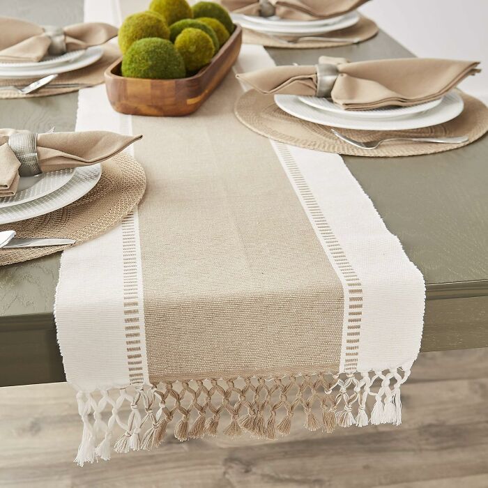Neutral-toned table runner with tassels, set on a dining table with plates and decorative moss balls for Black Friday deals.