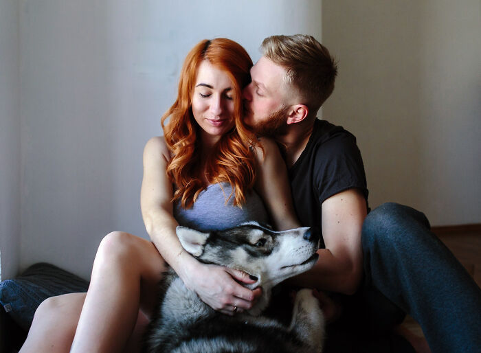 A woman and man sitting on the floor with a large husky dog, showing most insane dog mom things in a cozy moment.