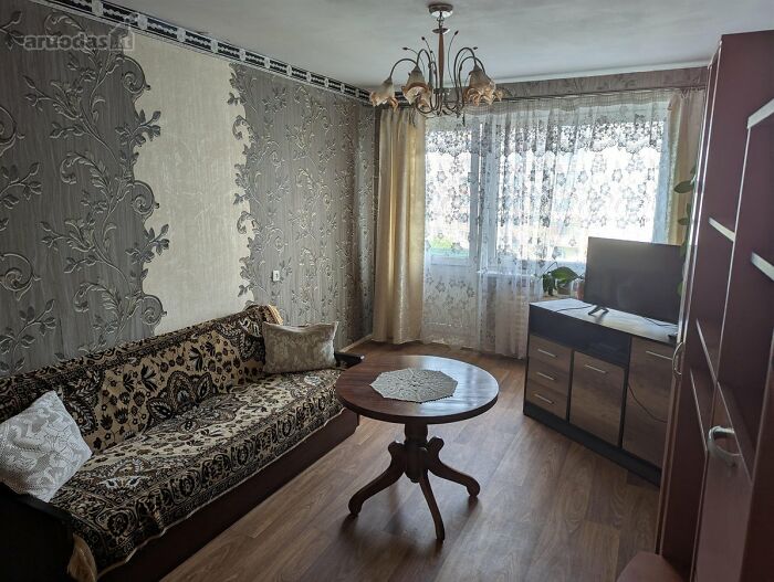 Living room with patterned sofa, wooden table, TV cabinet, and floral wallpaper in a wild real estate listing.