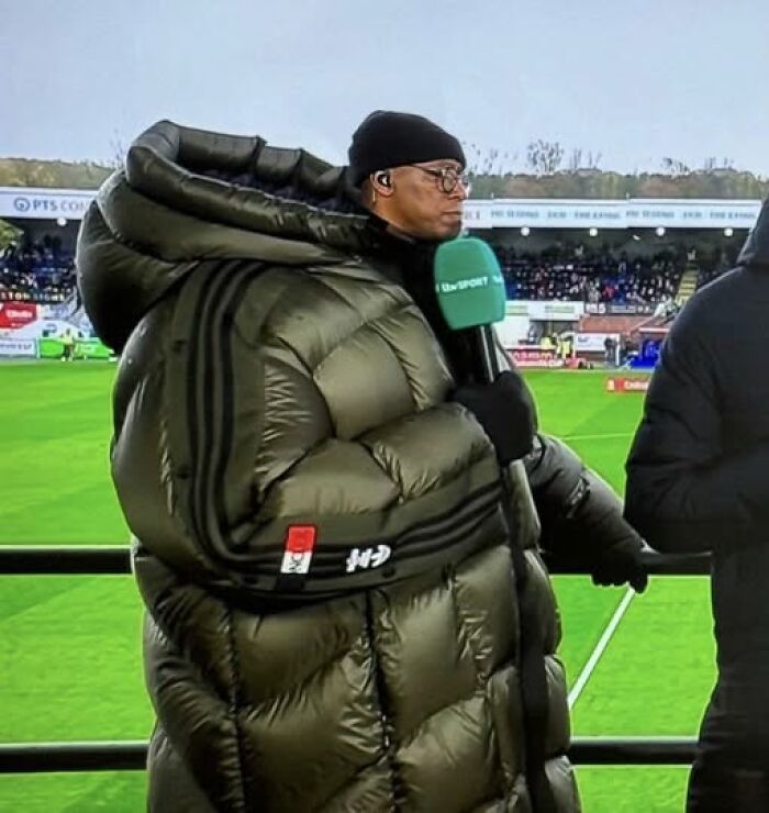 Man wearing an oversized puffer jacket holding a microphone during a sports event, a pic that goes hard and stands out.