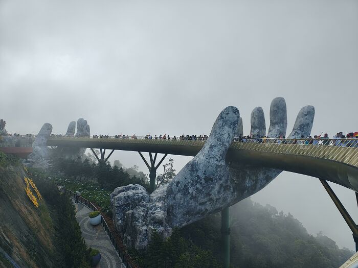 Pedestrian bridge held by giant stone hands in a misty mountainous area, illustrating Miami travel expectations.