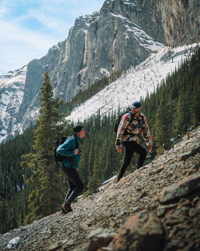 Two hikers climbing a rocky mountain trail surrounded by trees and snow, reflecting on purpose and life journey.