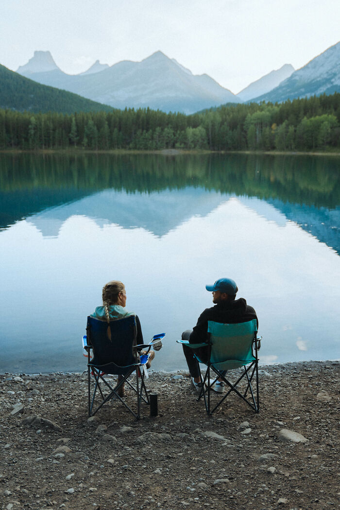 Two people sitting by the lake in camping chairs with mountain reflections, symbolizing a journey toward finding purpose.