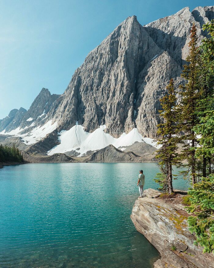 Person standing by a lake surrounded by mountains and trees, reflecting on purpose on a journey of self-discovery.