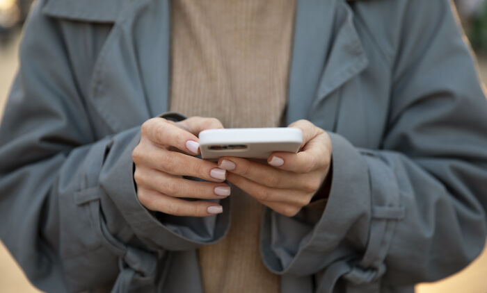 Person wearing a gray coat and beige sweater holding a smartphone, reflecting on a relationship with their brother after 20 years apart