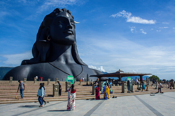 Massive black sculpture of a meditating figure with visitors around, showcasing spectacular sculptures for travel bucket lists.