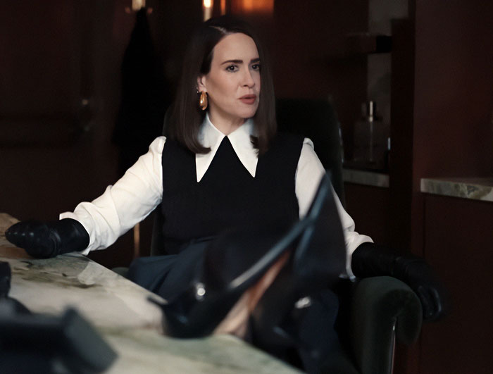 Woman in black and white outfit sitting with feet on table during alleged painful All's Fair premiere with Kim Kardashian.