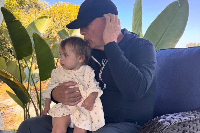 Bruce Willis sitting outdoors holding a young child, showing a tender moment amid his dementia journey update.