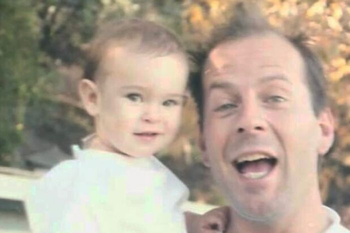 Bruce Willis smiling and holding a baby outside, illustrating a family moment amid dementia update discussion.