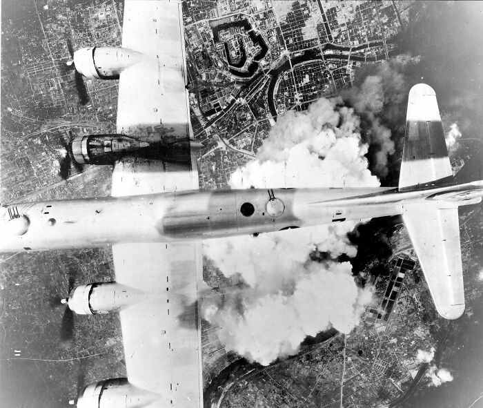 Aerial view of a bomber plane releasing smoke over a city, illustrating the butterfly effect in real life events.