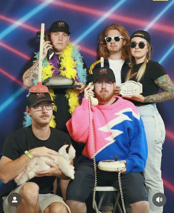 Group of five posing in an awkward studio pic with retro props, colorful outfits, and playful expressions, showcasing awkward studio vibes.