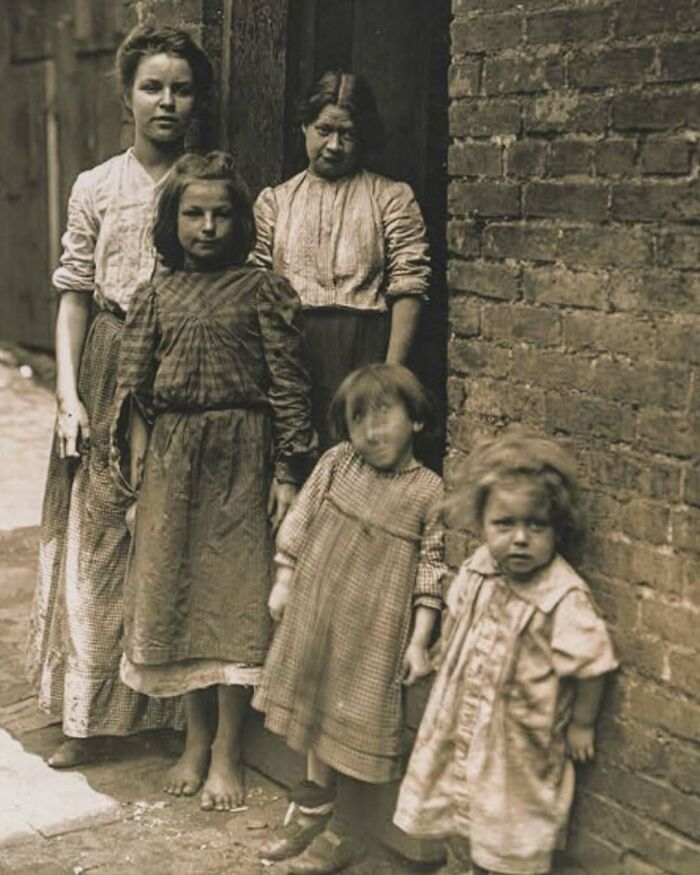 Group of barefoot Victorian era children standing in an alleyway wearing worn clothes, showcasing weird Victorian era photo style.