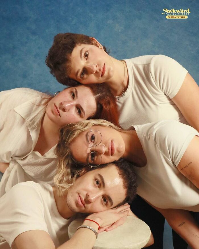 Four people in awkward studio pics posing with heads stacked closely against a blue backdrop, wearing casual light-colored clothing.