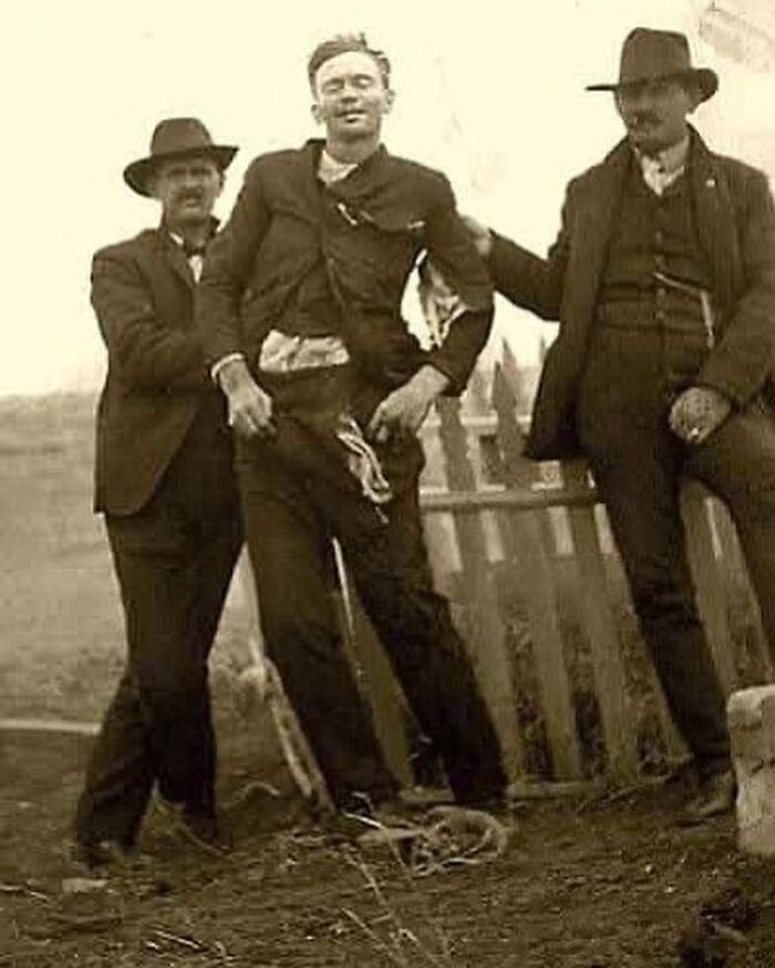 Three men in Victorian era clothing posing outside near a broken fence in a weird photo from the Victorian era.