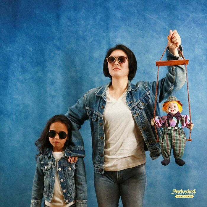 Woman and child in denim jackets wearing sunglasses posing with a clown puppet in an awkward studio pic.