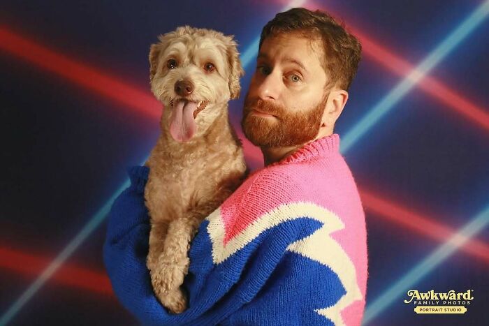 Man in colorful sweater holding happy dog in an awkward studio photo with retro laser background and smiling expressions