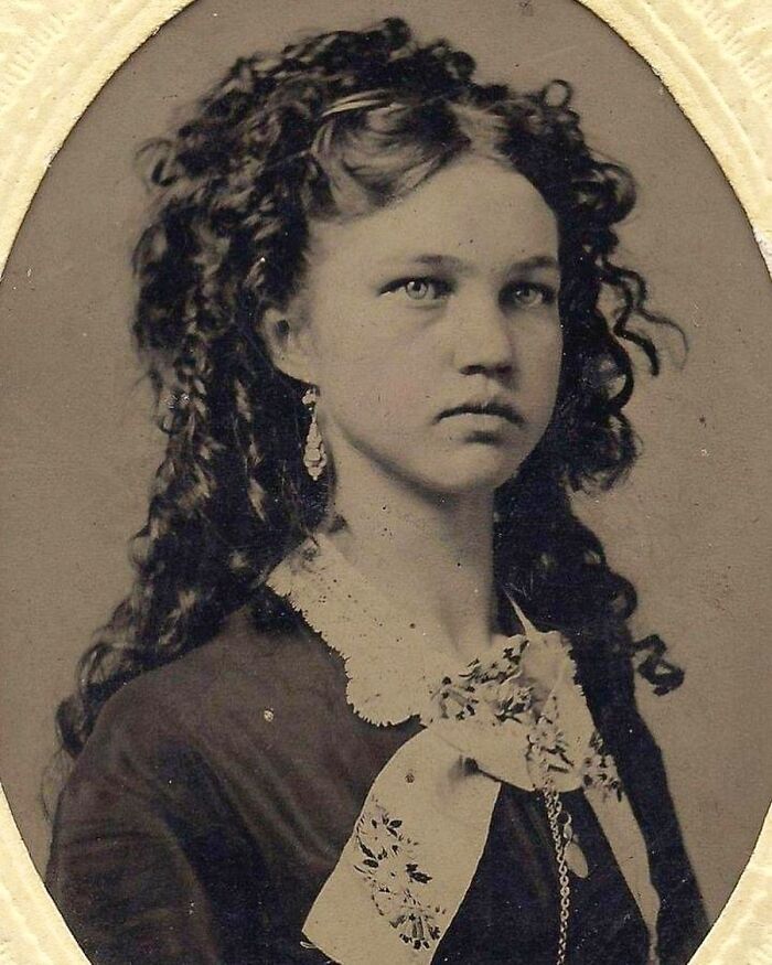 Victorian era portrait of a young woman with curly hair, wearing vintage clothing and a lace collar.