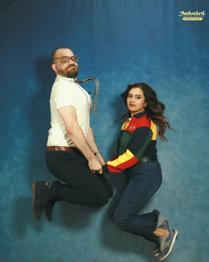 Man and woman holding hands and jumping in a studio, captured in one of the awkward studio pics with a blue background.