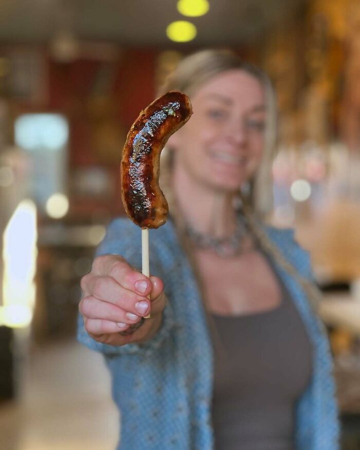 Woman holding grilled sausage on a skewer, representing funny steak and lobster complaints about juiciness and buttery taste.